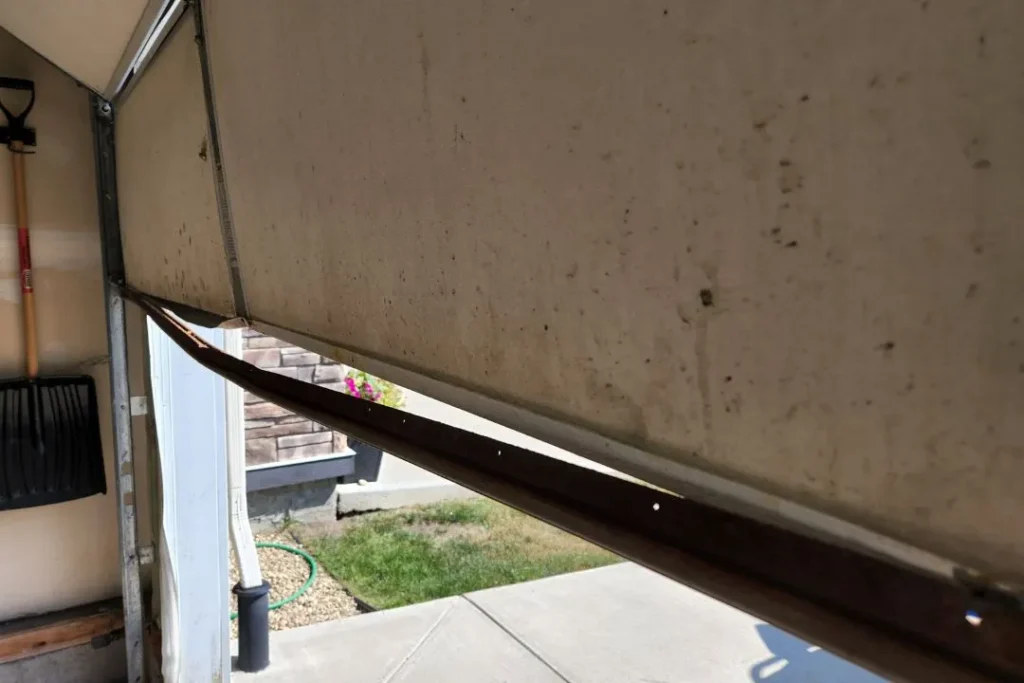 Inside view of a garage door with a bent and cracked bottom Rubber needing repair.