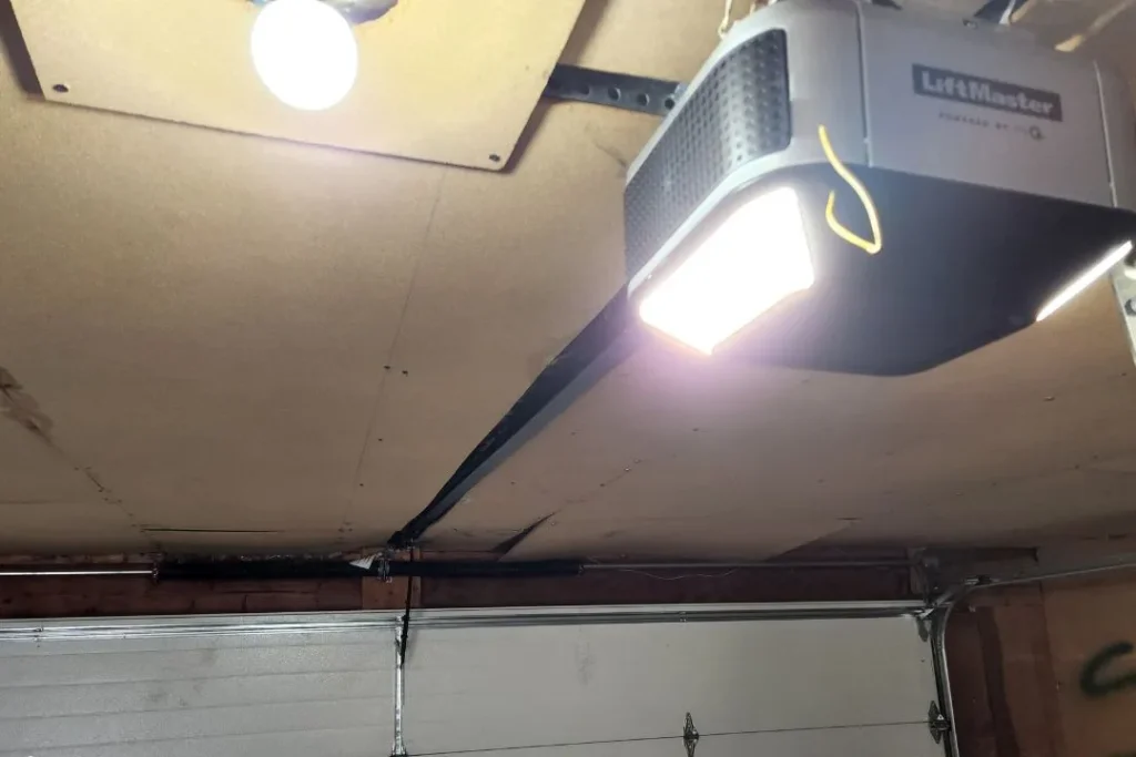 Close-up of a ceiling-mounted LiftMaster garage door opener with light on, installed in a residential Leduc garage.