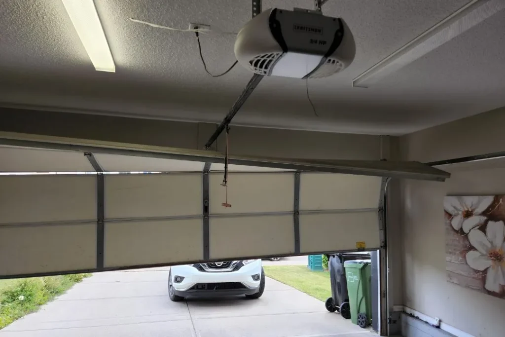 Garage door panel sagging on one side due to possible spring or cable failure.